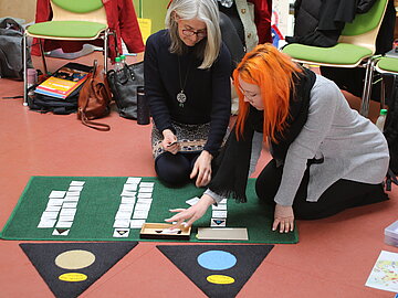 Teilnehmer:innen legen Montessorimaterial auf Teppich